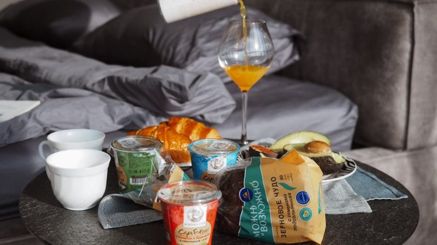Cozy breakfast setup with croissant, juice, and yogurt on bedside table, creating a relaxing morning vibe.